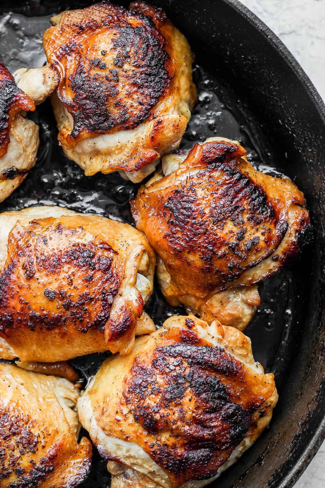 A close up of cooked chicken thighs in a cast iron skillet.