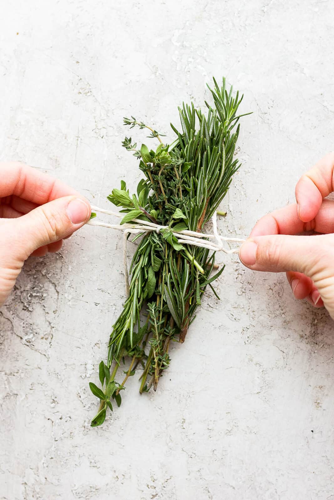 A bow being tied around fresh herbs with kitchen twine.