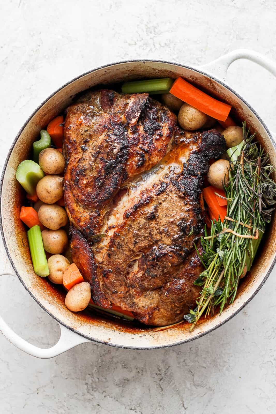 Herb bundle in a dutch oven with a pork roast and vegetables.