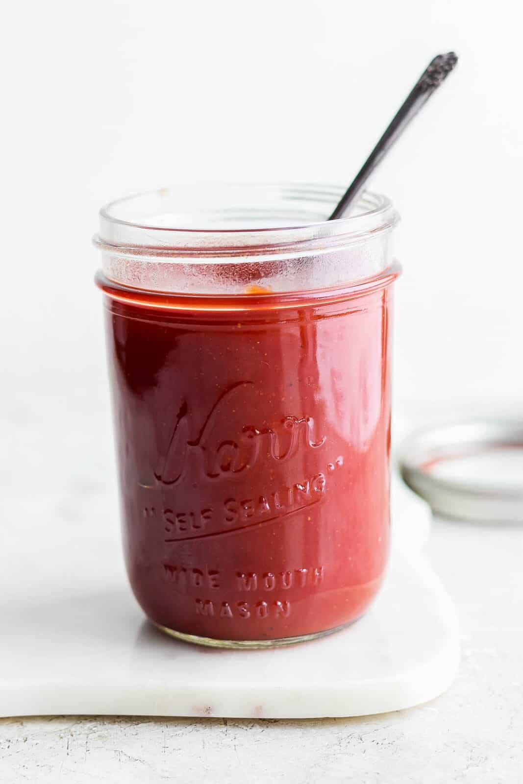 Jar of Homemade BBQ Sauce in a mason jar with a spoon sticking out of it. 