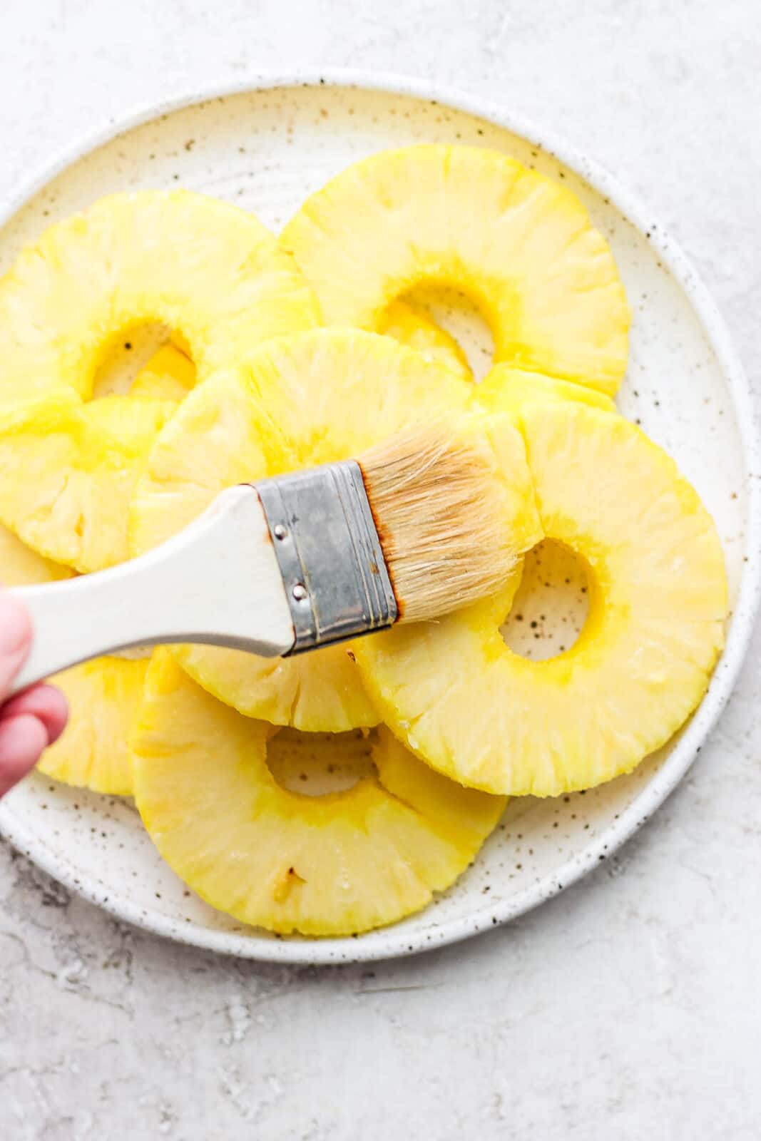Olive oil being brushed on pineapple slices.