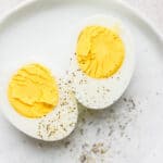 A hard boiled egg cut in half with salt and pepper on top.