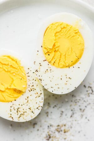 A hard boiled egg cut in half with salt and pepper on top.