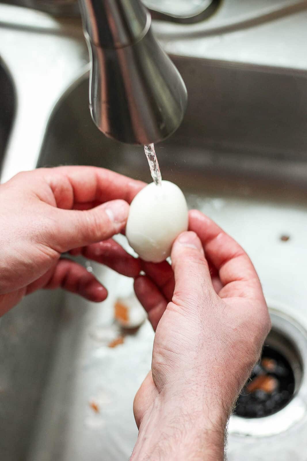 A fully peeled hard boiled egg under running water.