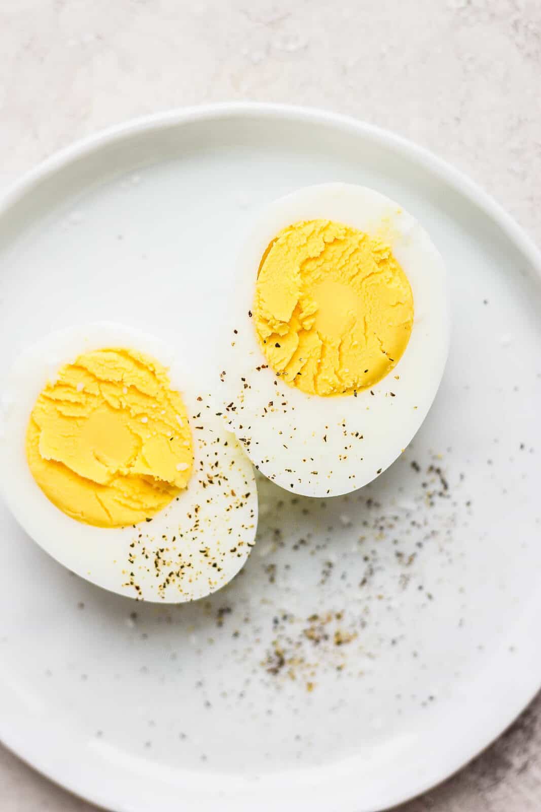 Hard boiled eggs cut in half on a plate with salt and pepper.