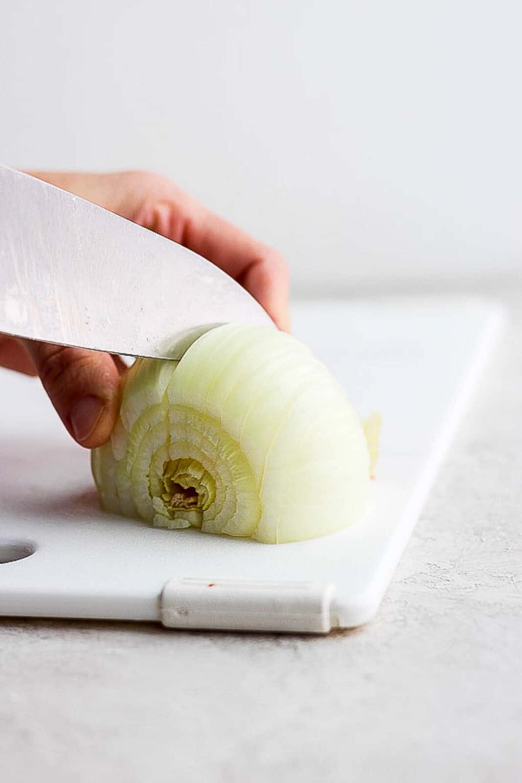 A knife slicing a yellow onion on a cutting board.