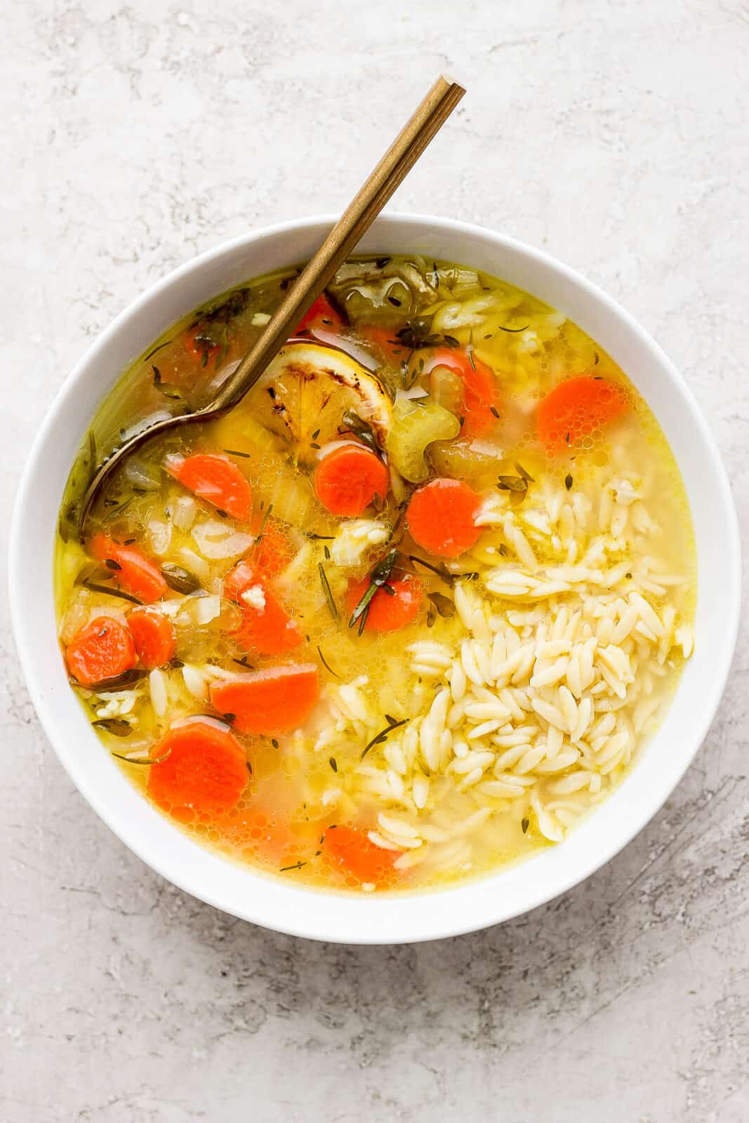 A bowl of lemon chicken orzo soup with a spoon.