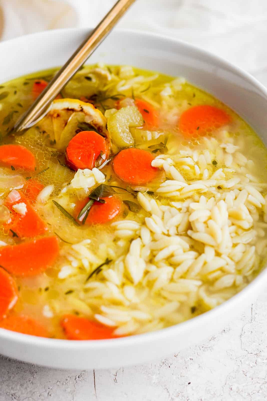 A bowl of lemon chicken orzo soup with a spoon.