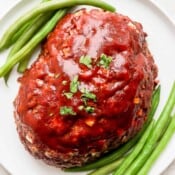 Meatloaf with a meatloaf glaze on top on a plate with green beans.