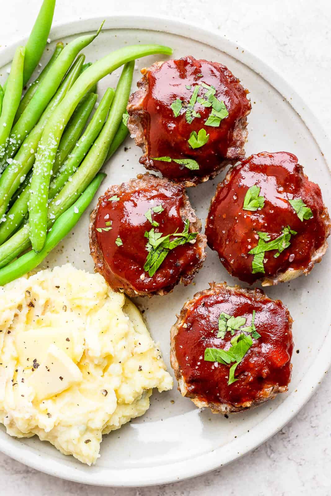 Plate of meatloaf muffins with green beans and mashed potatoes.