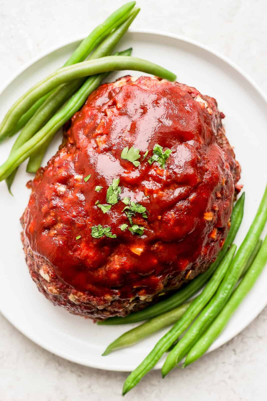 A smoked meatloaf with a meatloaf glaze on top on a plate with green beans.