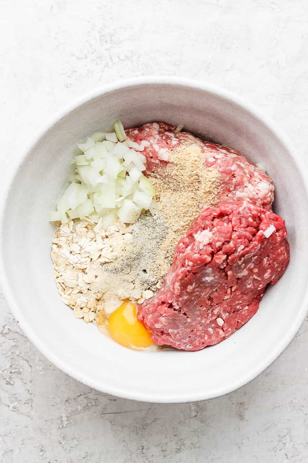 A bowl of ingredients for meatloaf with the seasoning on top. 