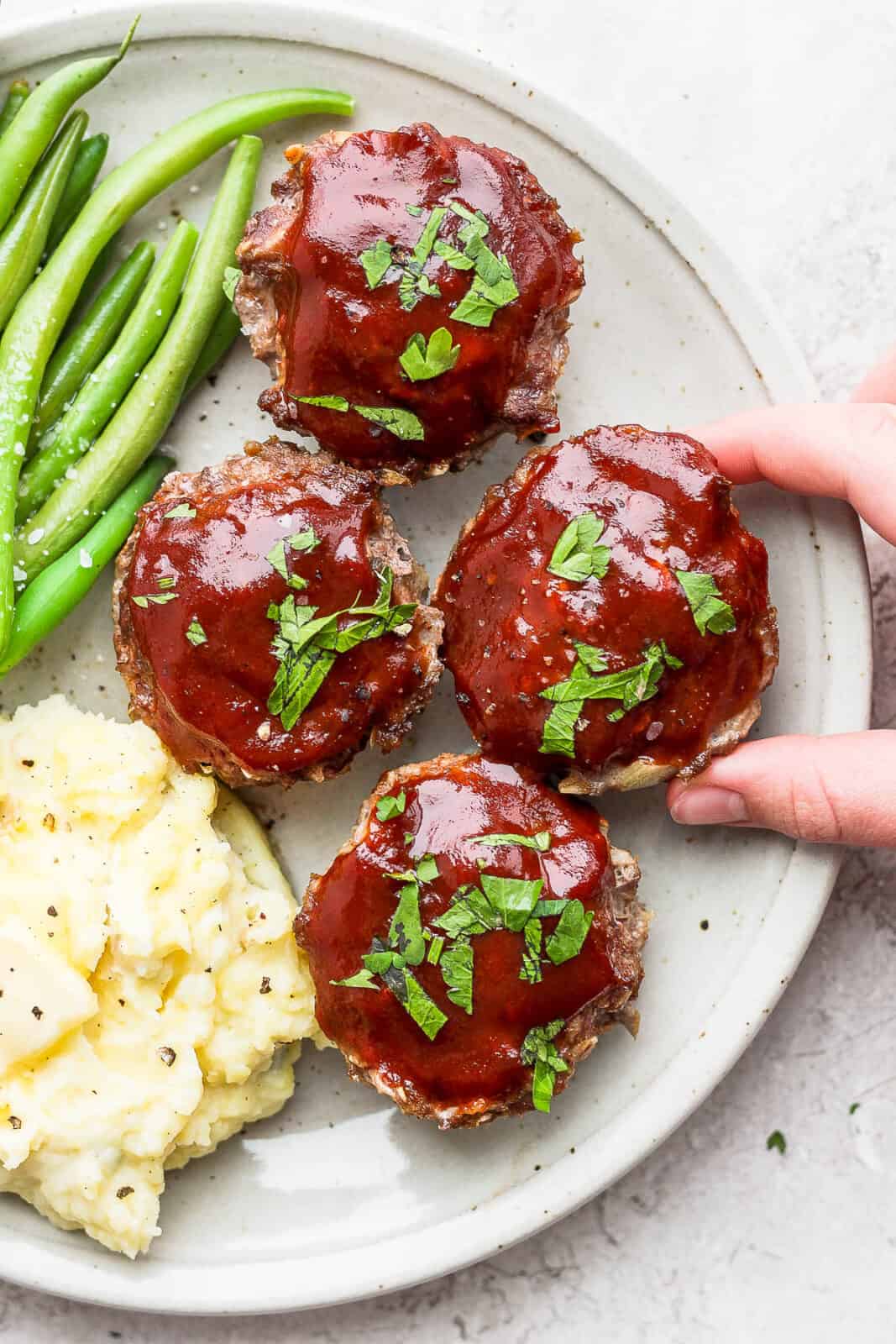 Plate of mini meatloaf muffins with glaze on a plate with mashed potatoes and green beans.
