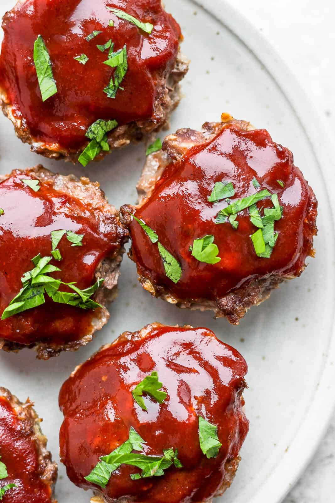 Mini meatloaf on a plate with glaze on top and garnished with fresh parsley.