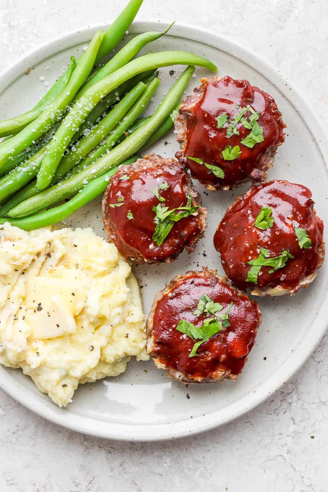 Plate of mini meatloaf muffins with glaze on a plate with mashed potatoes and green beans.