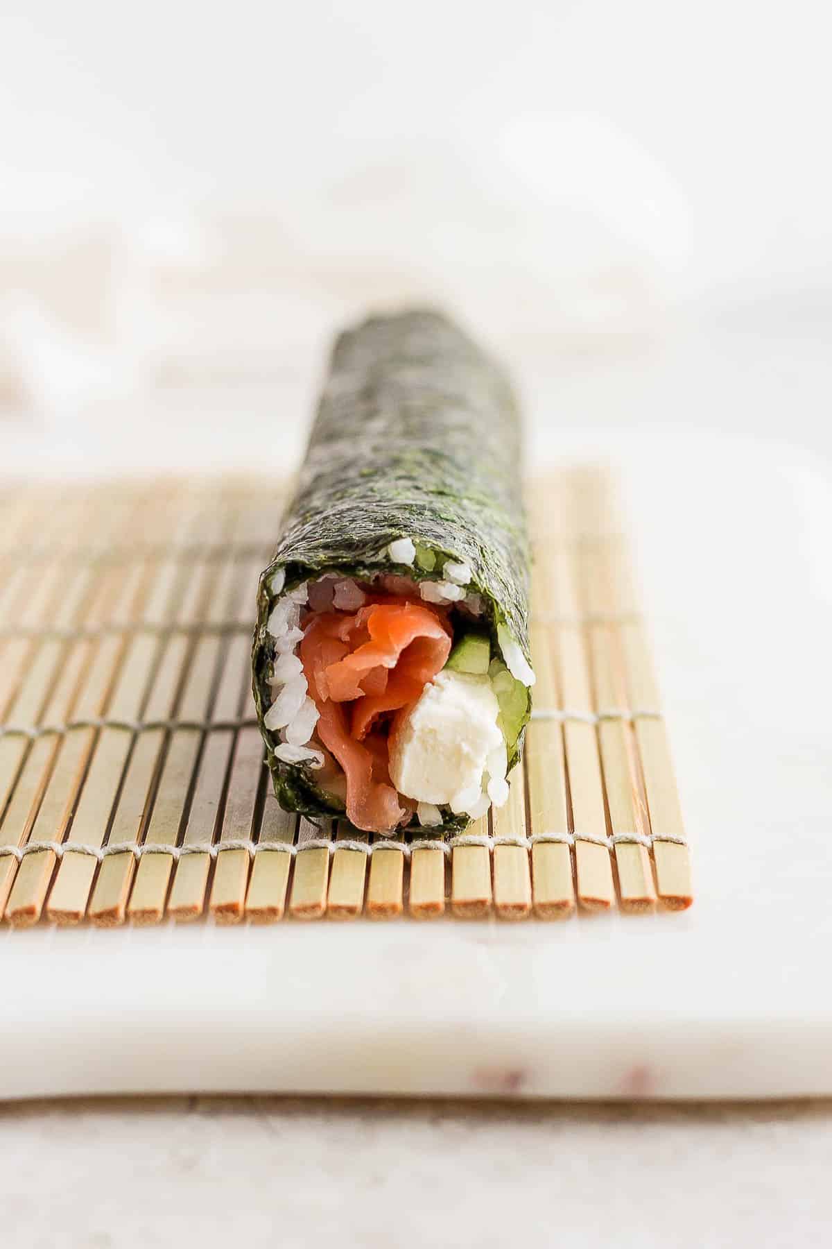 A secure philadelphia roll on top of a bamboo sheet.