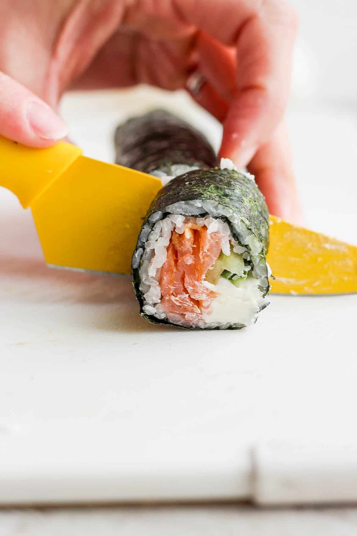 A sharp knife cutting the philadelphia roll into pieces.