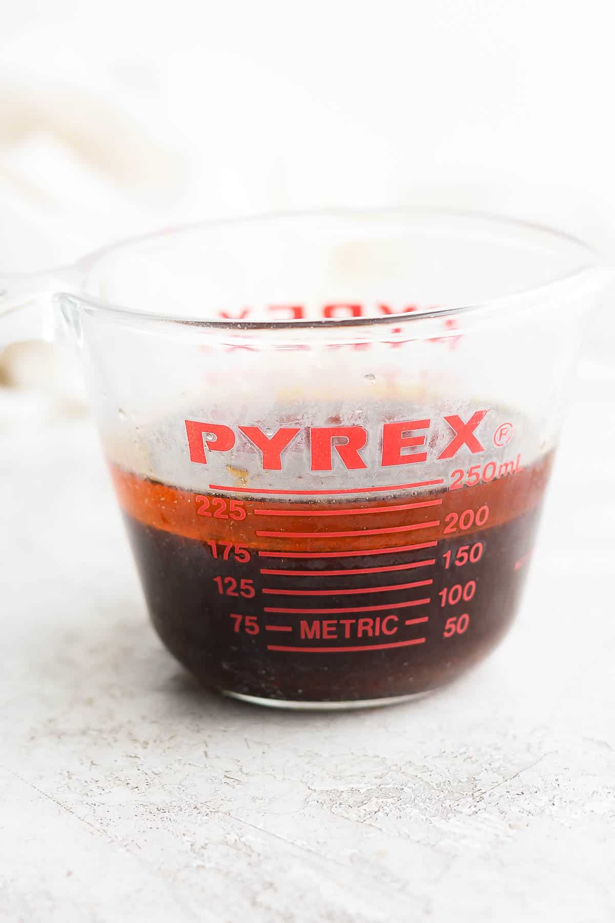 Side angle of a glass measuring dish filled with pork drippings and a little layer of fat on the top. 