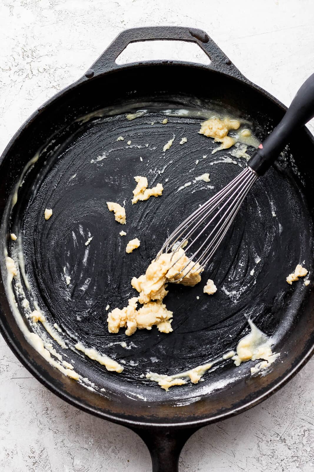 A cast iron skillet with a roux inside and a whisk. 