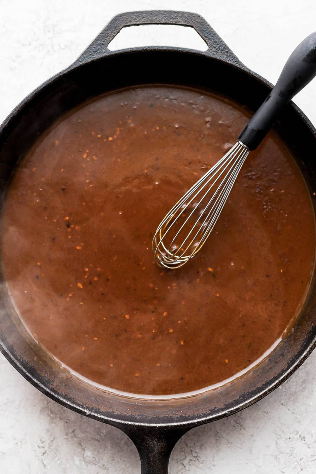 A cast iron skillet with pork gravy on the inside and a whisk. 