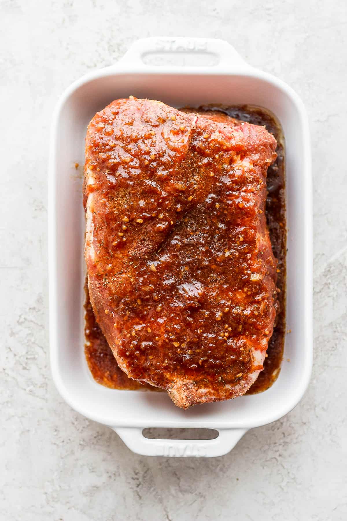 A pork roast in a marinade in a baking dish. 