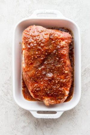 A pork roast in a baking pan covered in pork roast marinade.