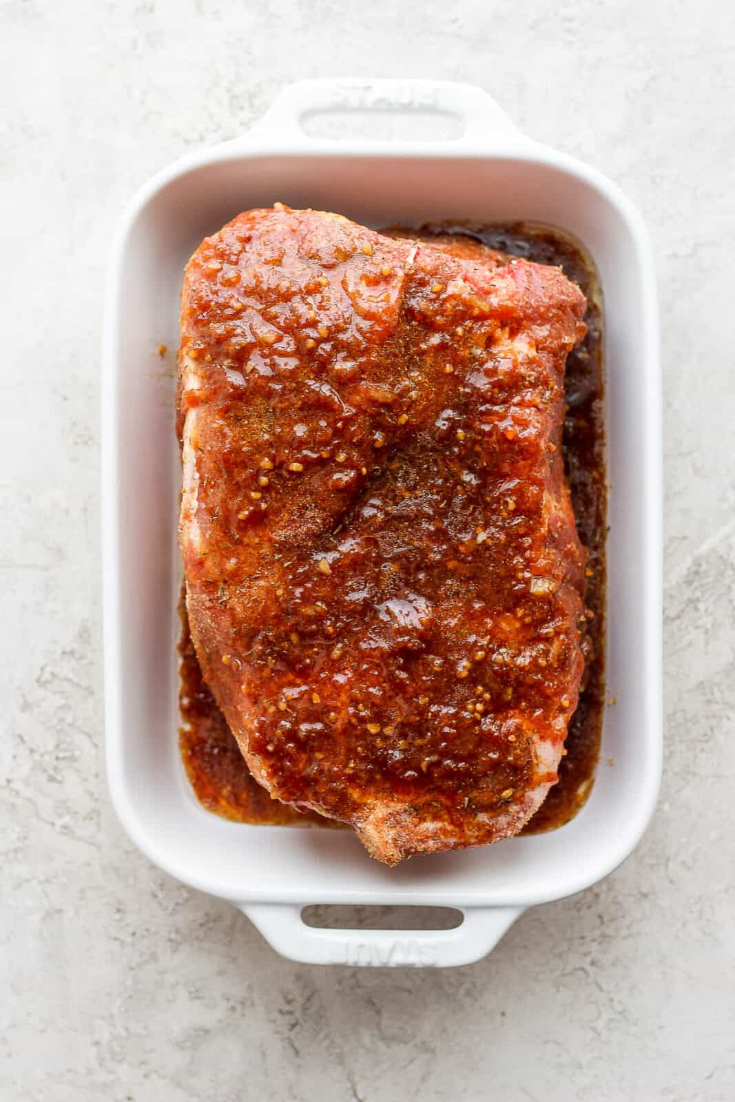 Pork roast covered in seasoning and marinade in a dish.