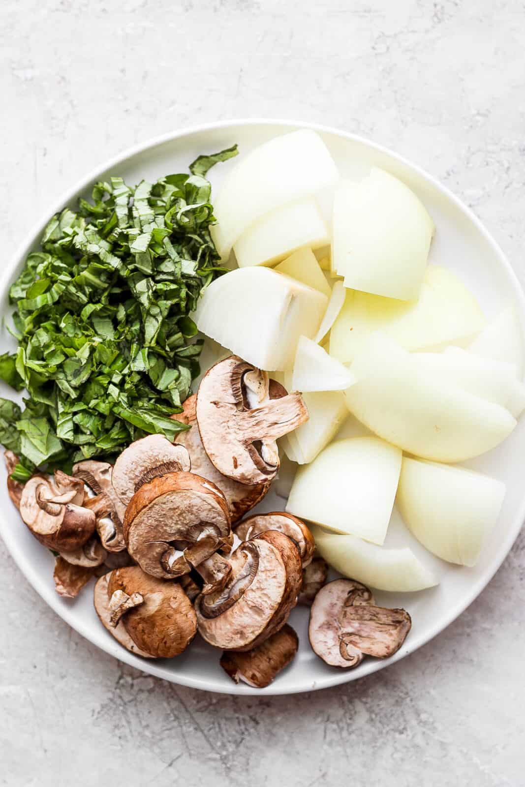 Chopped fresh basil, onion, and mushrooms on a plate.