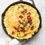 A cast iron skillet filled with smoked mashed potatoes and topped with cheese and bacon.