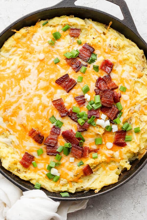 A cast iron skillet filled with smoked mashed potatoes and topped with cheese and bacon.