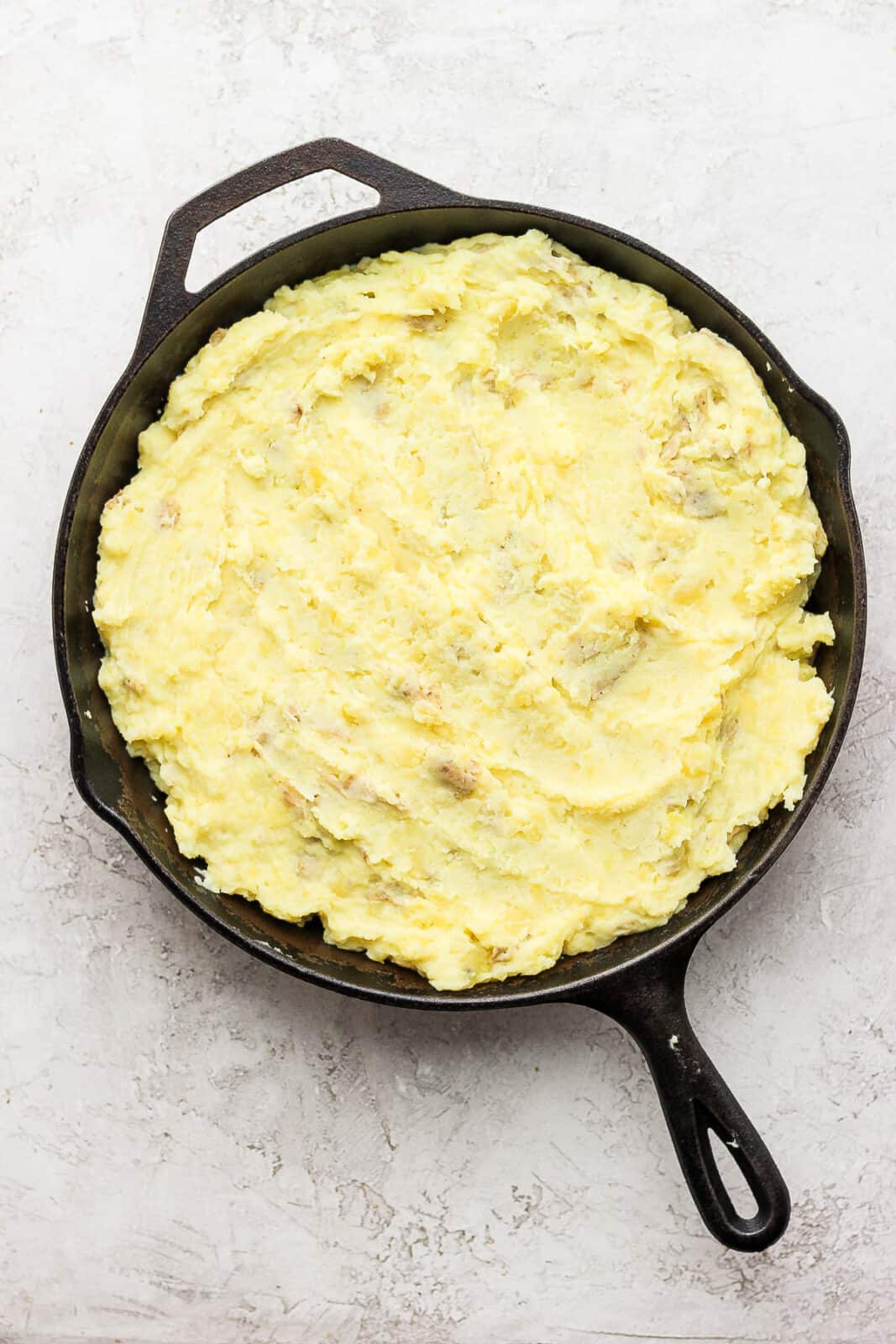 Mashed potatoes spread out evenly in a cast iron skillet. 