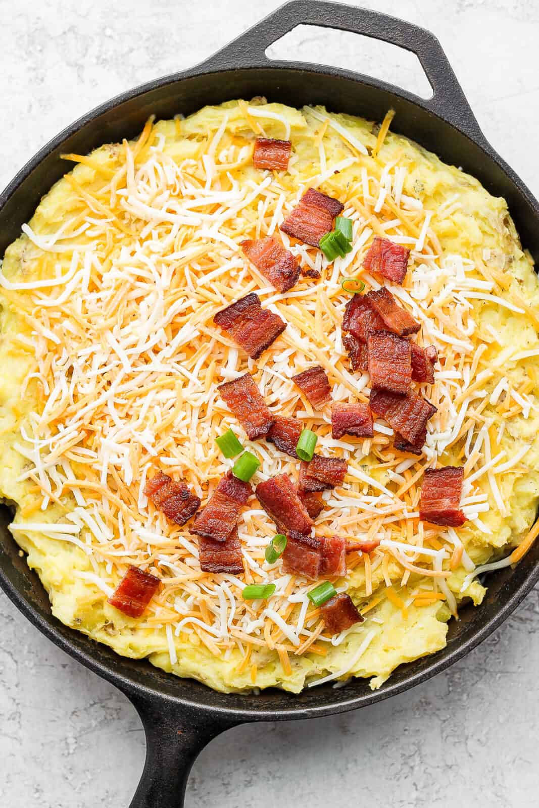 Smoked mashed potatoes in a cast iron skillet topped with cheese and bacon, before melting.