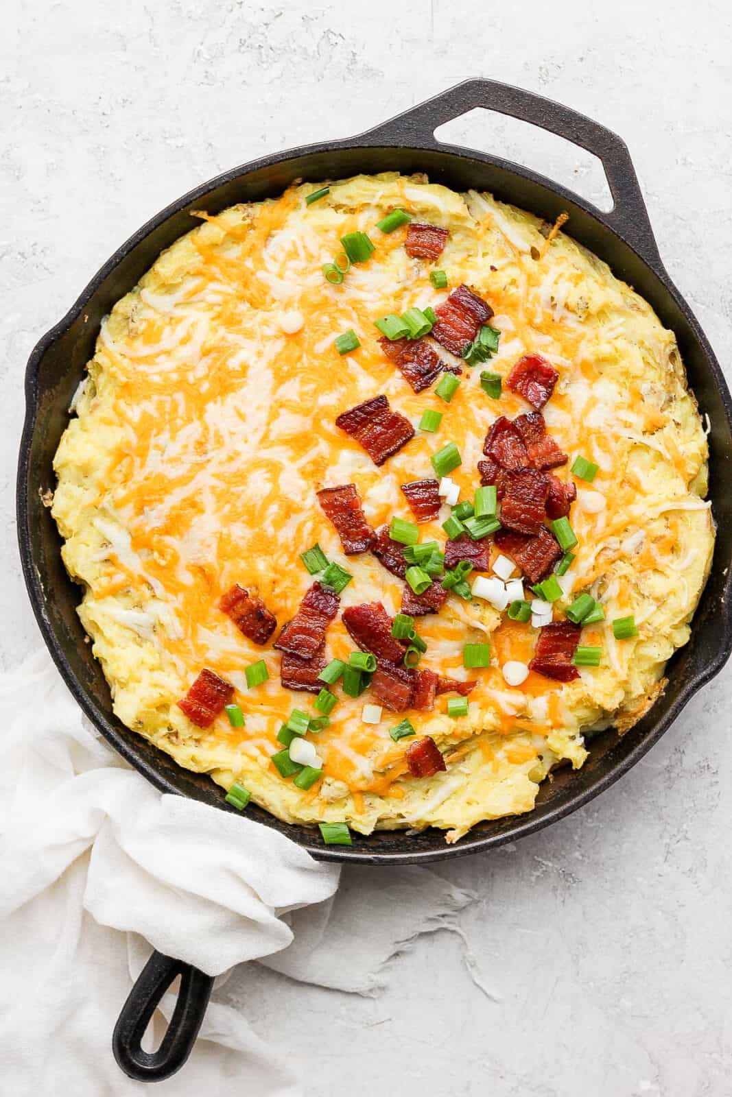 Cast iron skillet filled with smoked mashed potatoes and topped with melted cheese, bacon and green onion.
