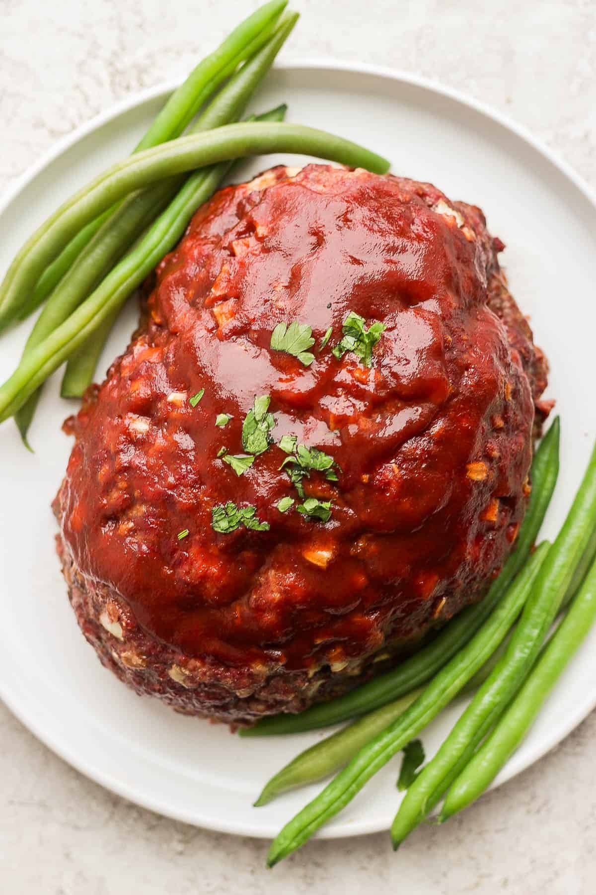 Top view of a smoked meatloaf on a plate with green beans on either side.