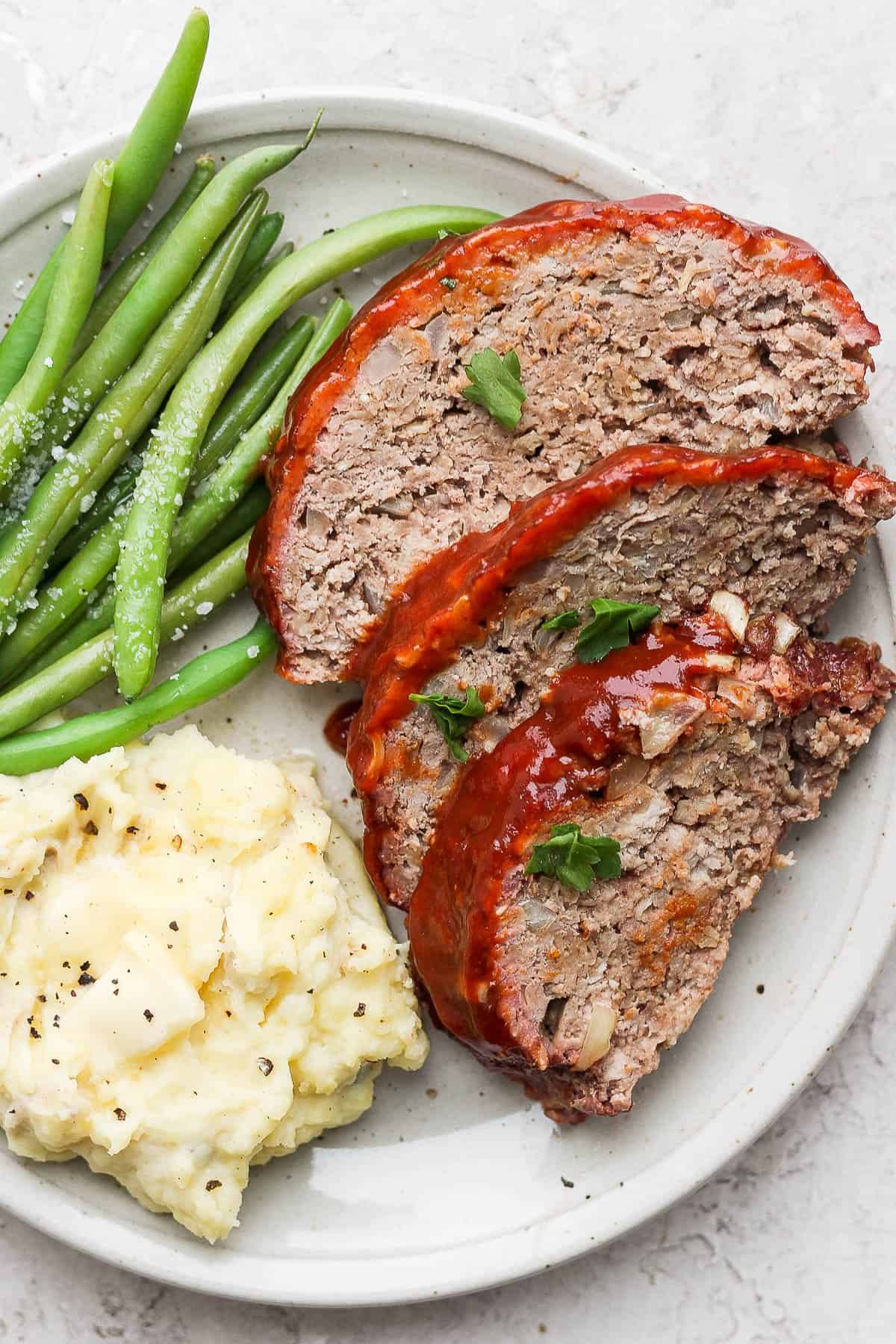 Plate of sliced smoked meatloaf, mashed potatoes and green beans.