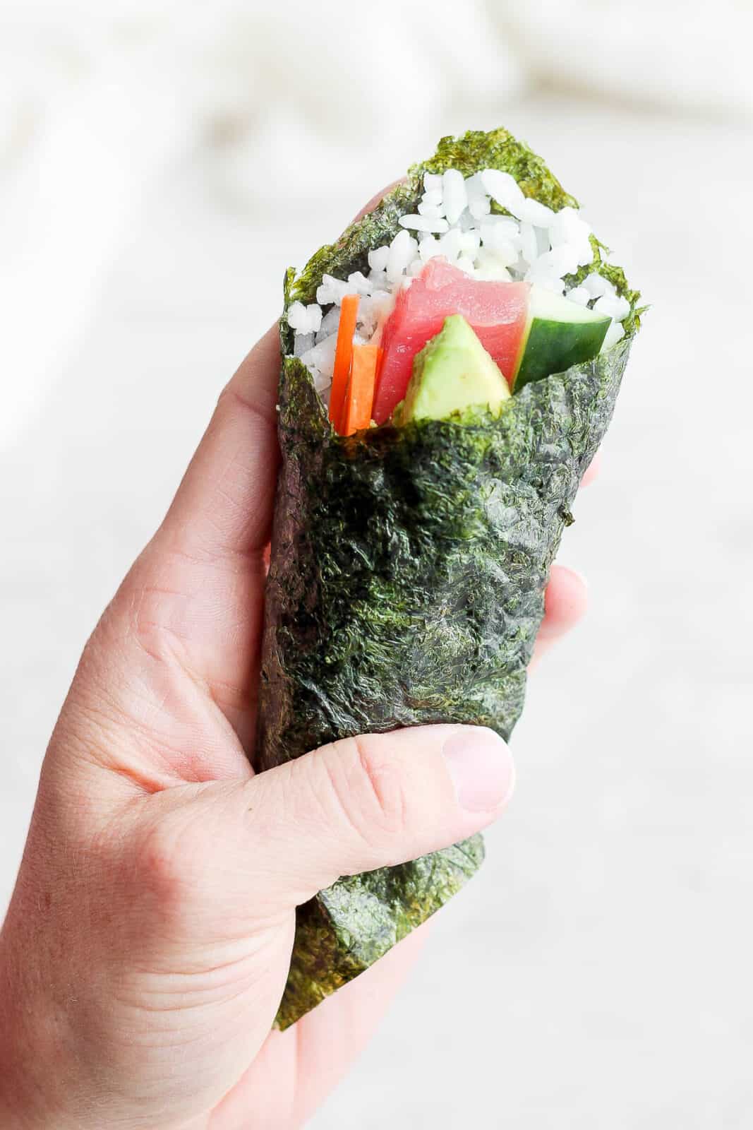 A hand holding a sushi hand roll.