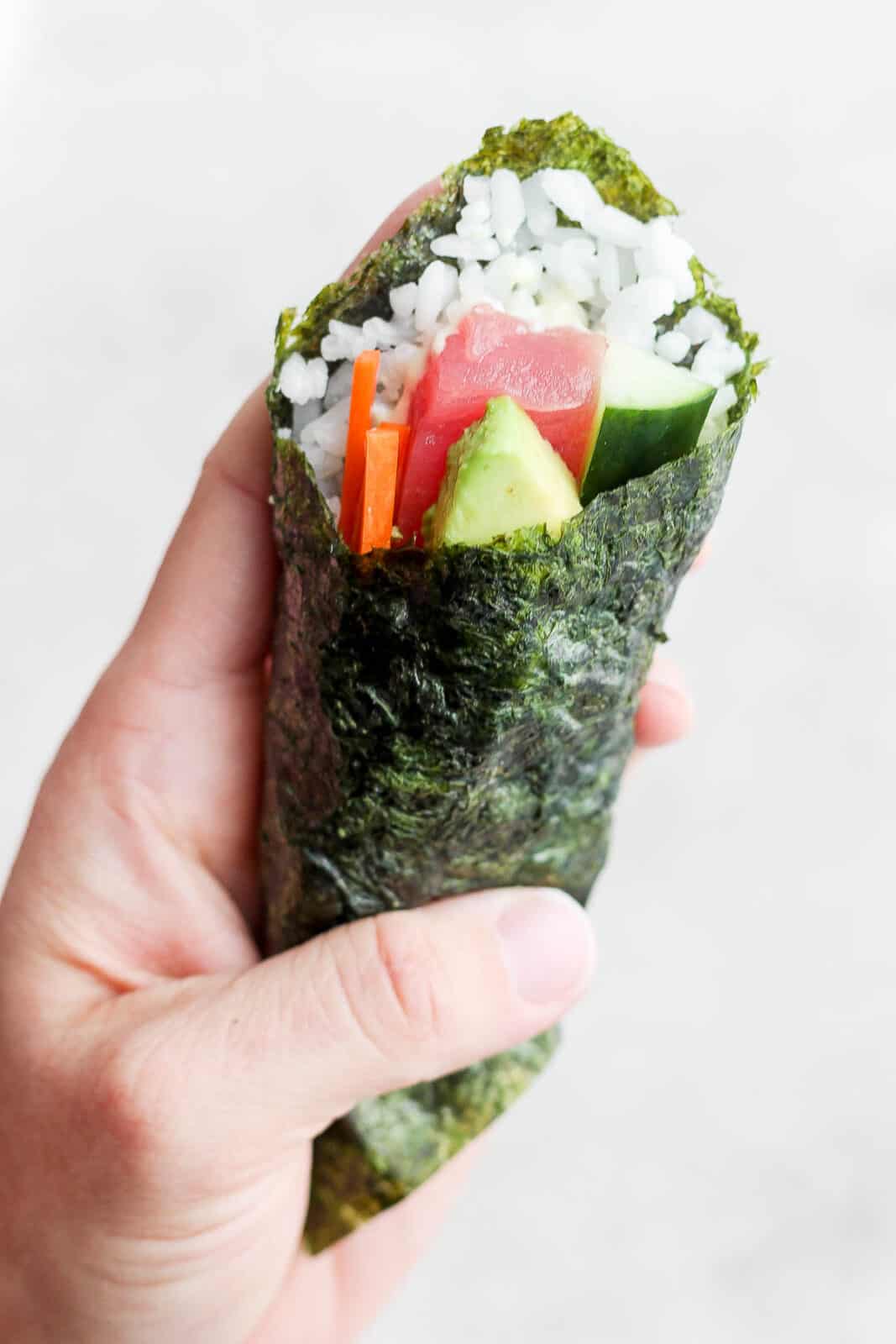 A hand holding a sushi hand roll.