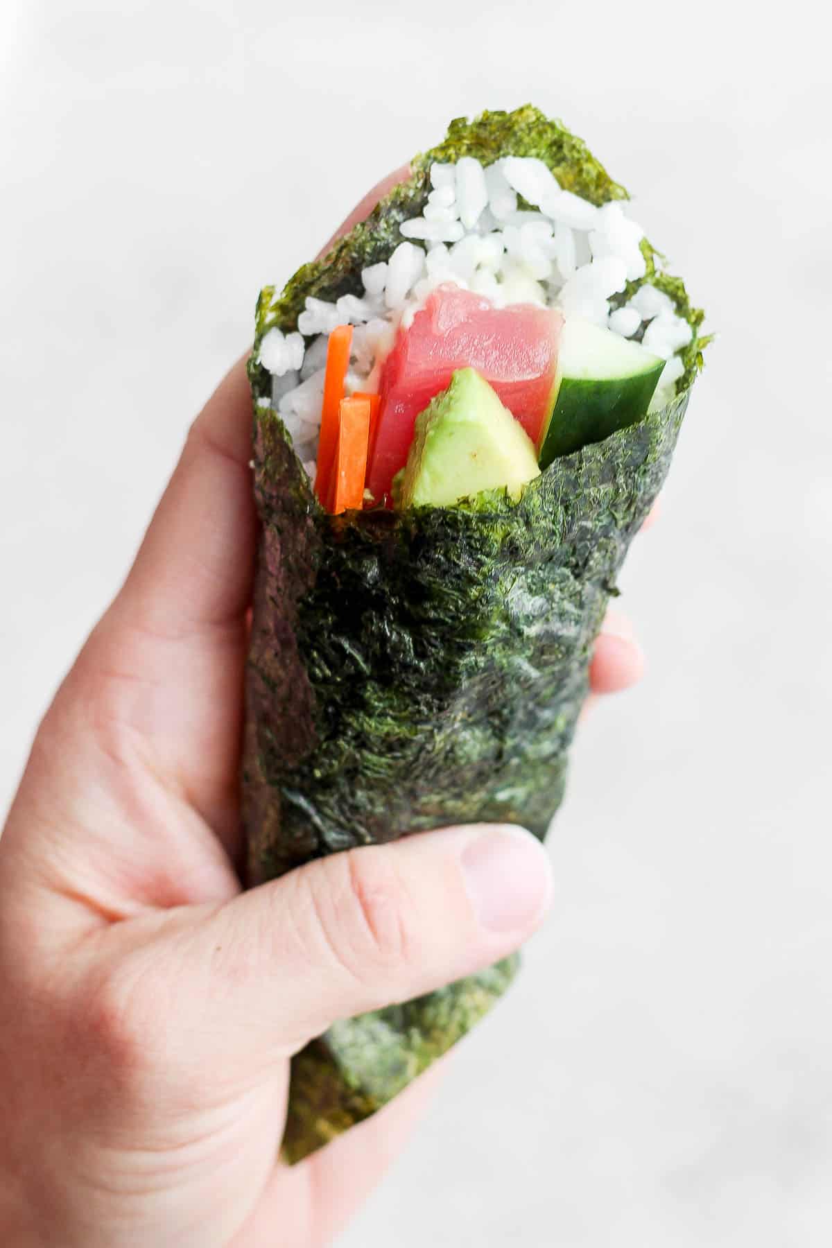 A hand holding a fully formed sushi hand roll.