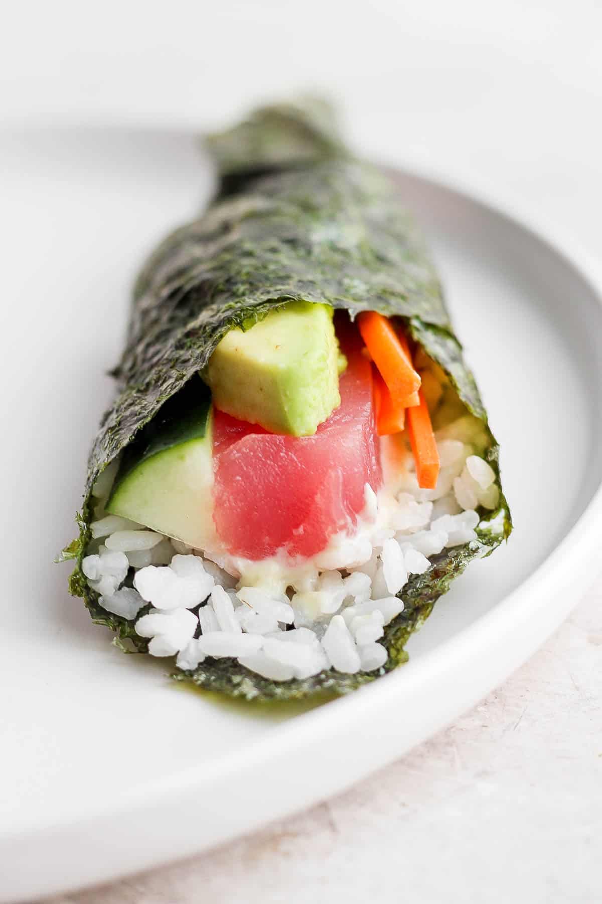 A sushi hand roll laying on a white plate.