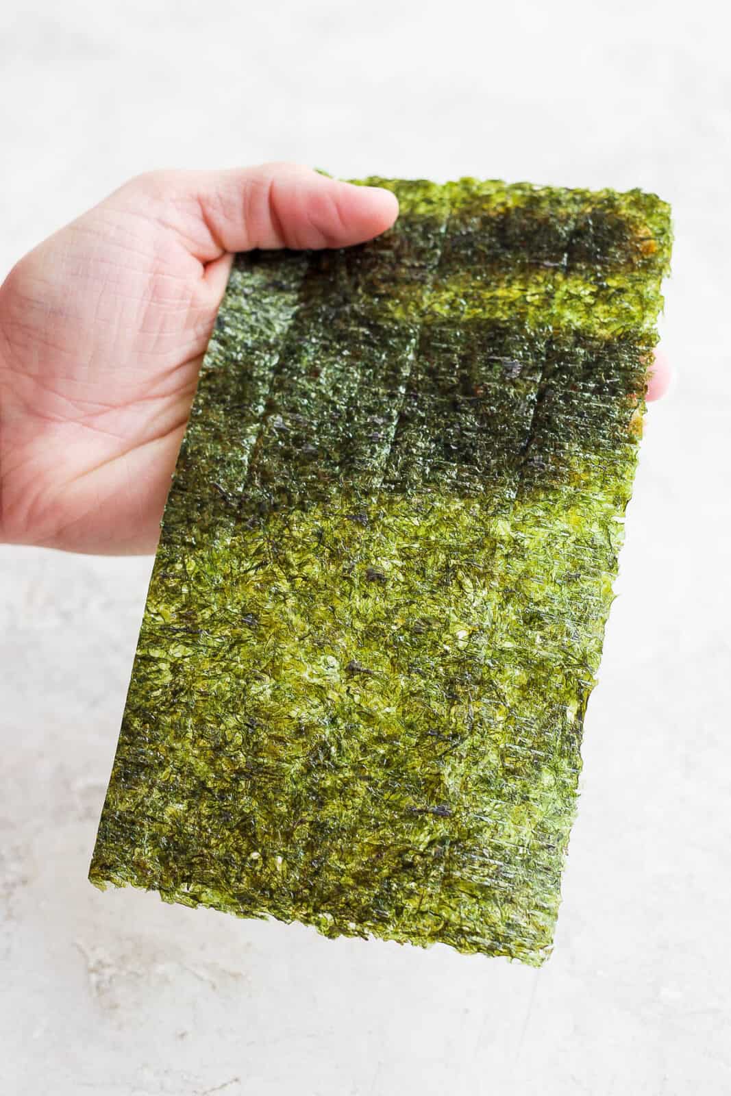 A hand holding half of a nori sheet.