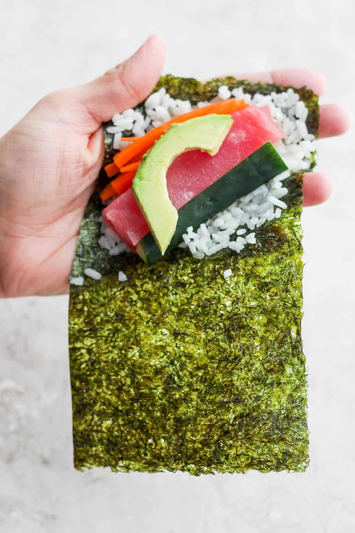 Cucumber, carrots and avocado added around a thick strip of tuna on a sushi hand roll.
