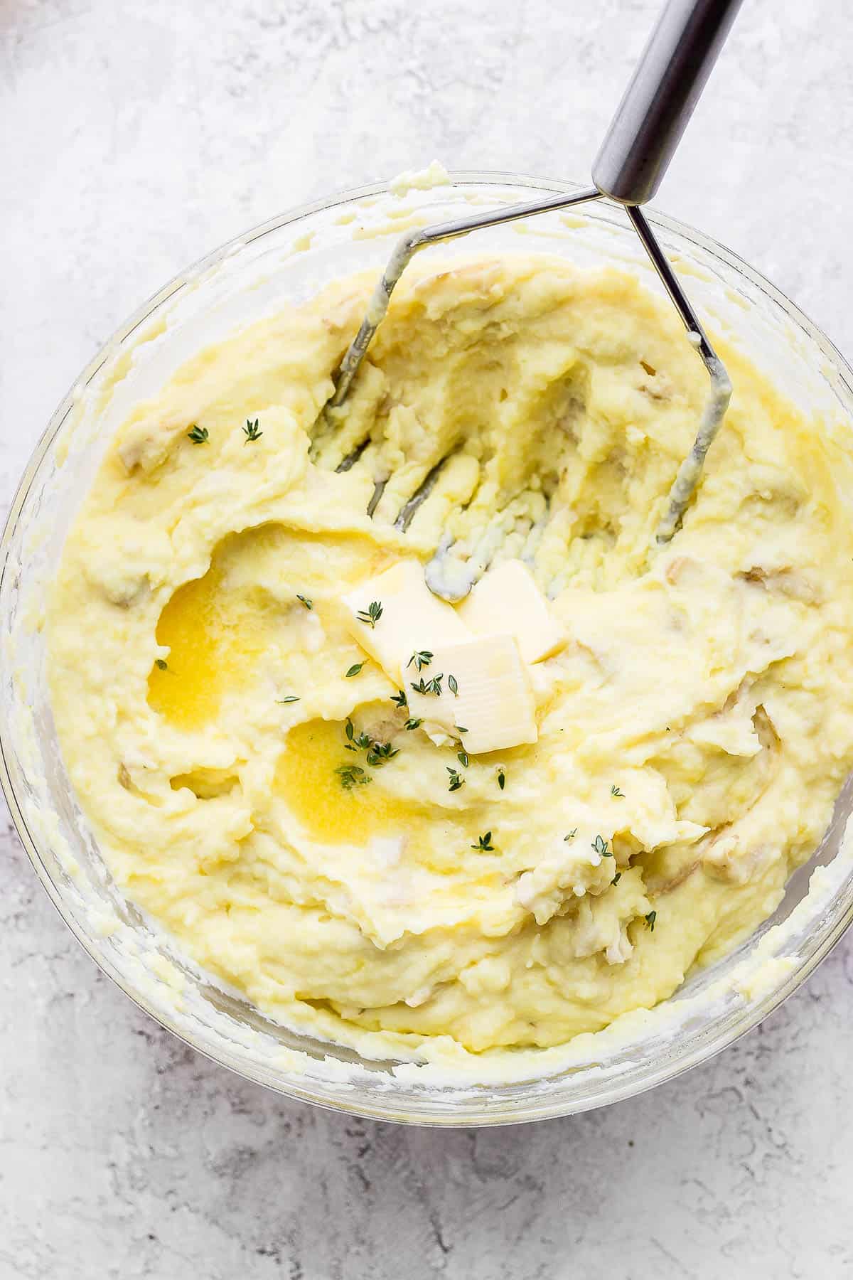 Yukon gold mashed potatoes in a bowl with a potato masher.