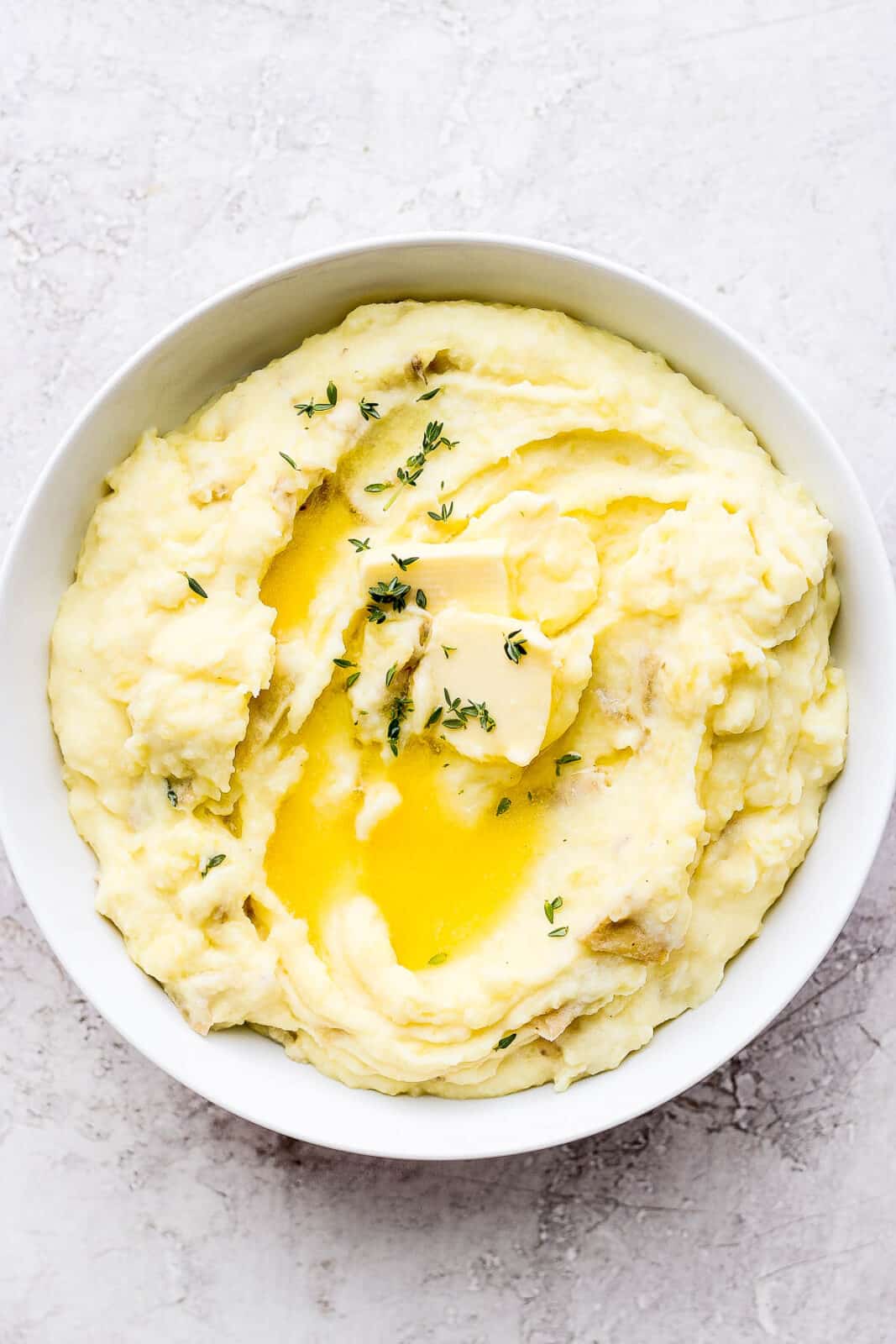 Bowl of ultimate yukon gold mashed potatoes with some butter and thyme on top.