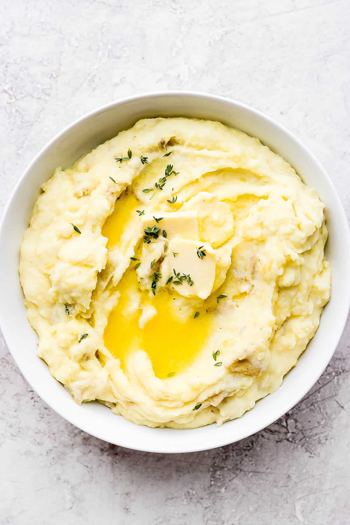 Bowl of ultimate yukon gold mashed potatoes with some butter and thyme on top.