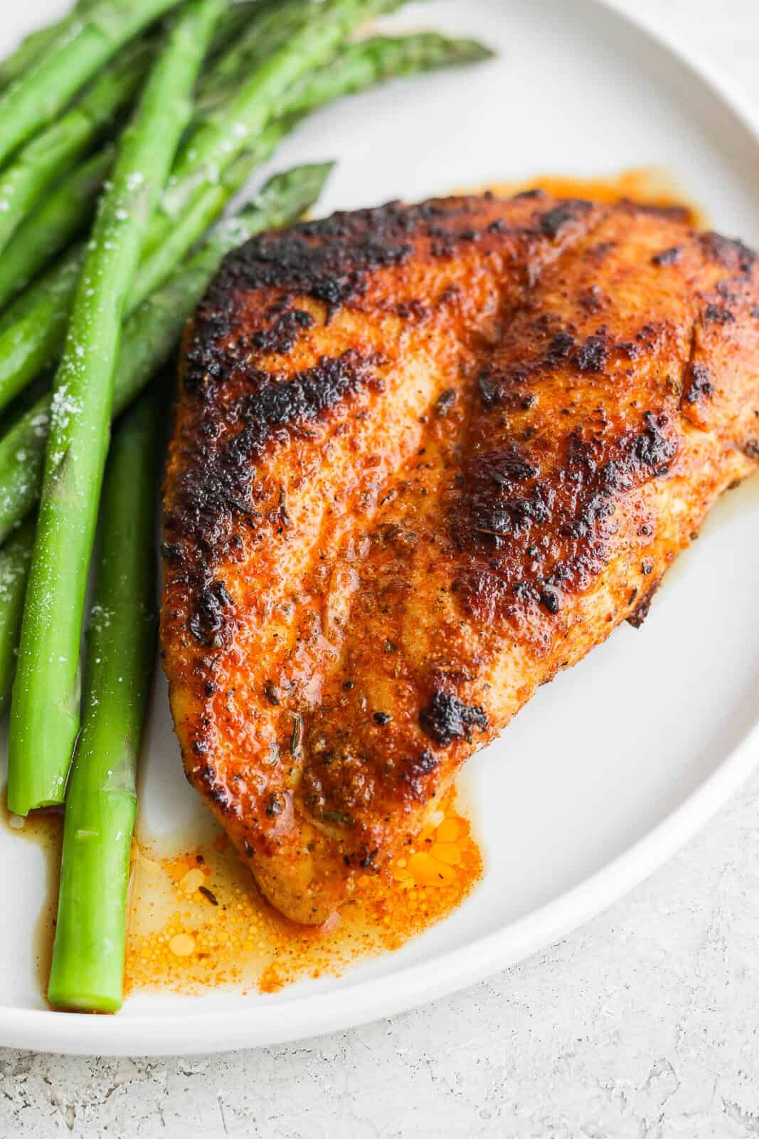 One blackened chicken breast on a plate with asparagus.