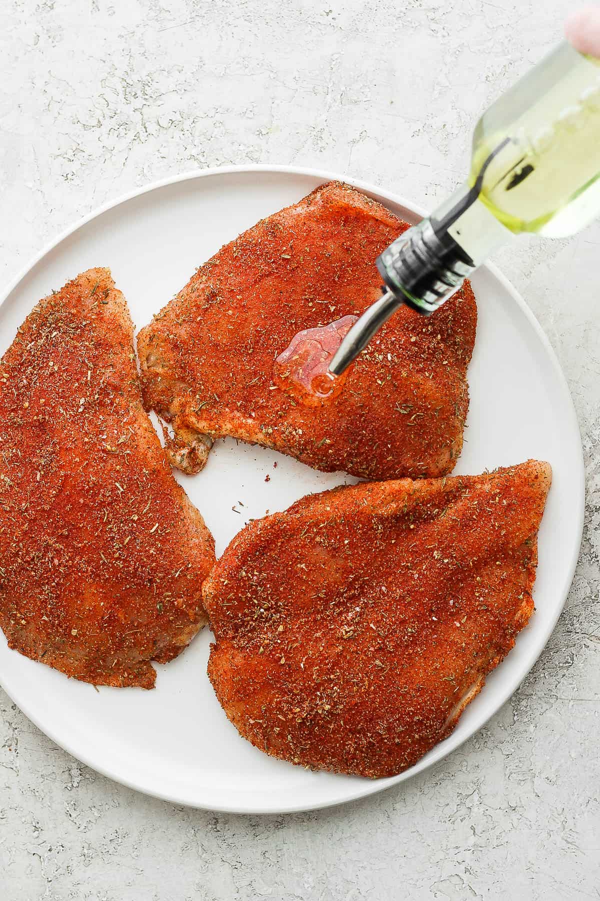 Olive oil being drizzled on the seasoned chicken breasts.