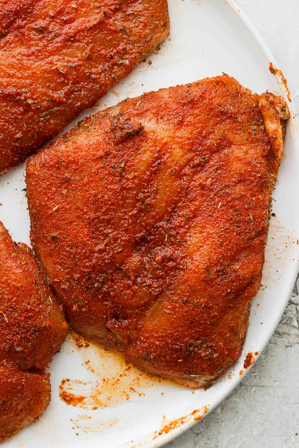 Chicken breasts on a plate with seasoning and oil rubbed on them.