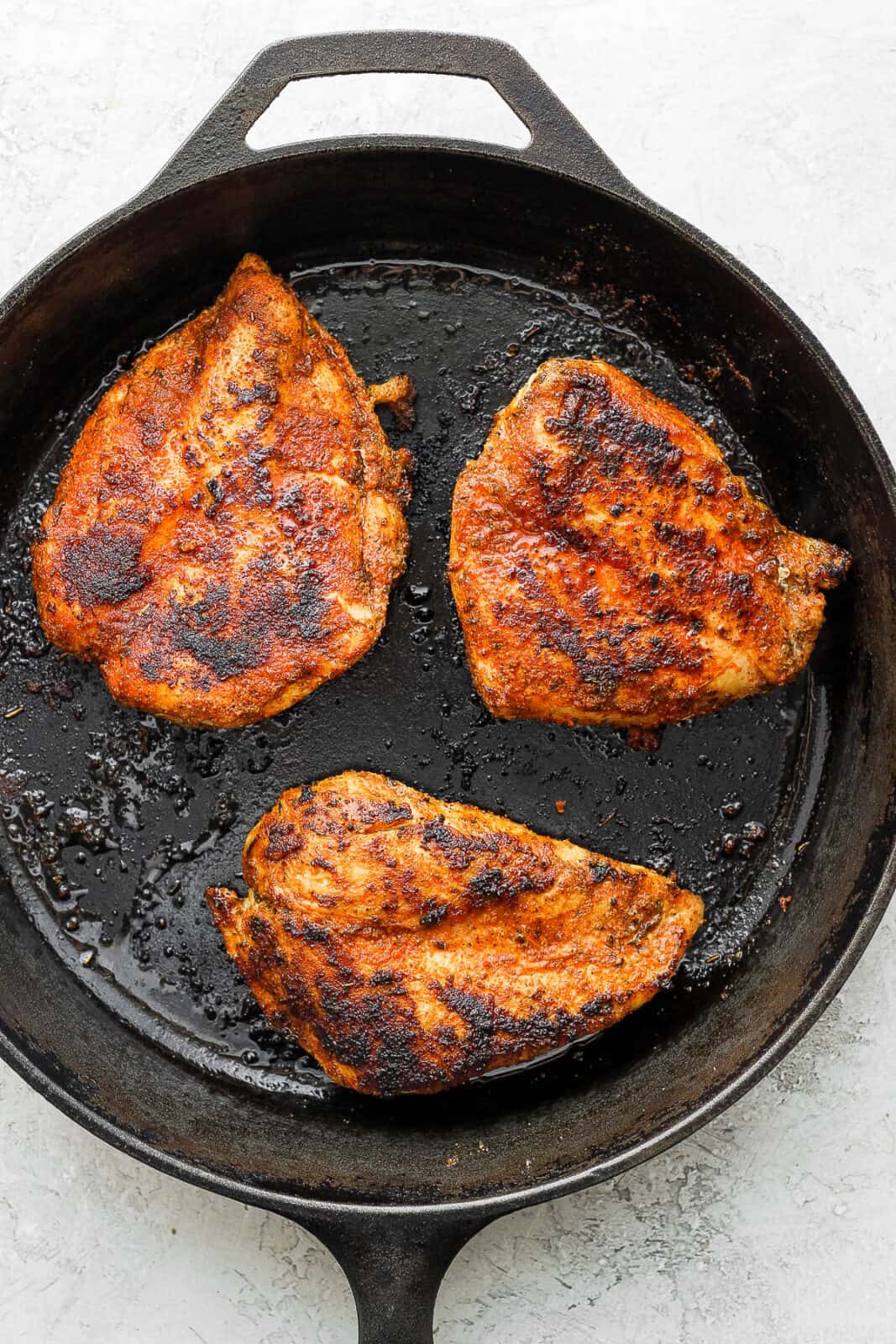 Blackened chicken breasts being seared in a cast iron skillet.