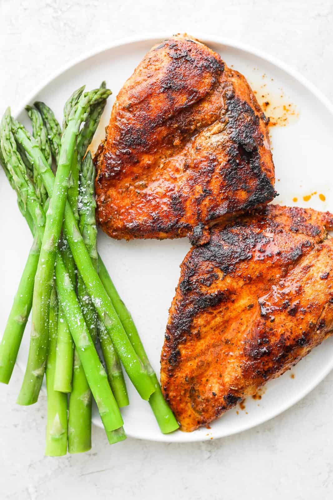 Blackened chicken breasts on a plate with asparagus.