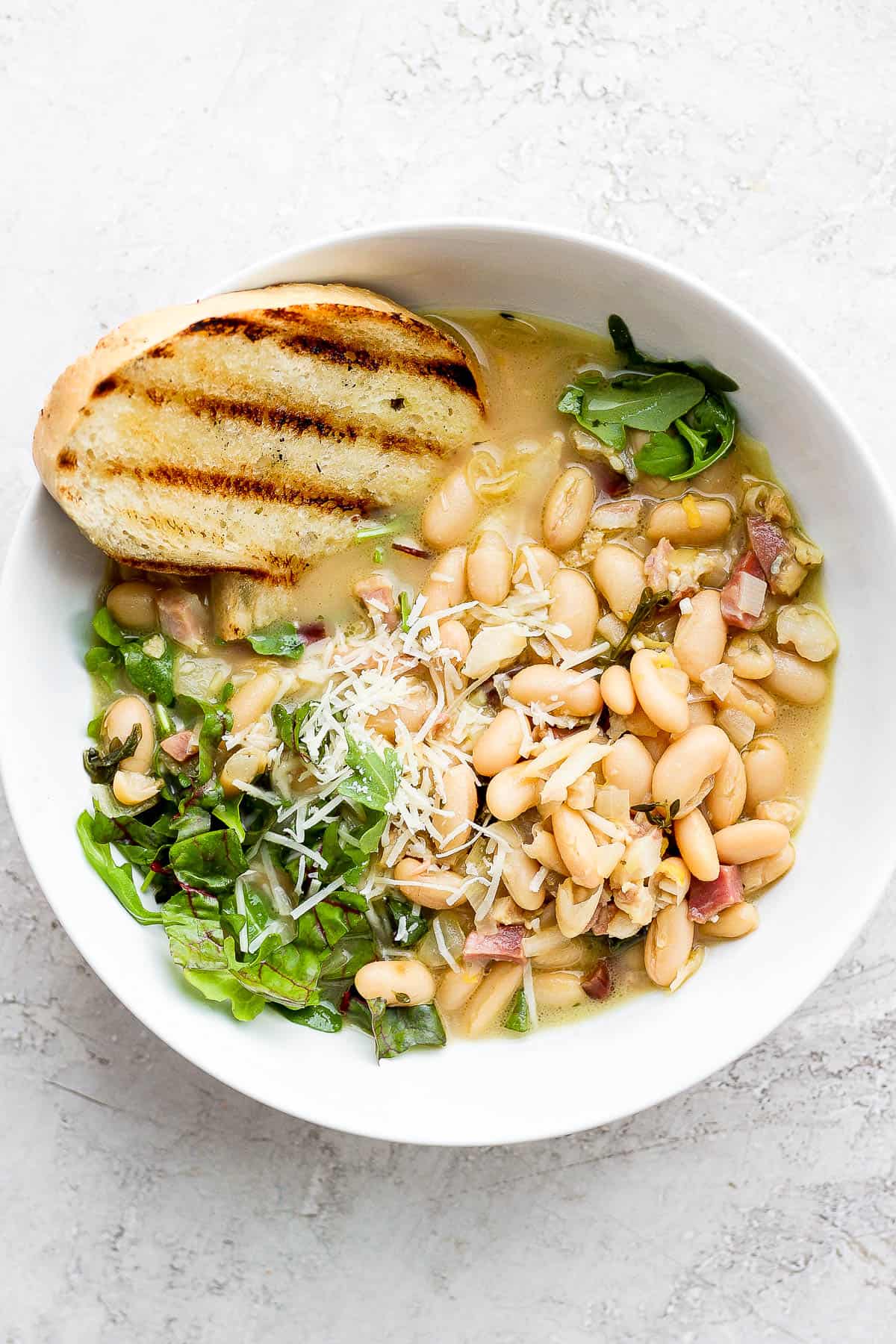 A bowl of brothy beans with a slice of grilled bread.